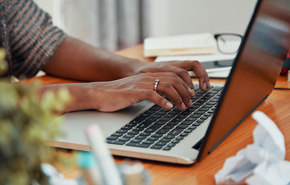 Faceless shot of modern black businesswoman working on laptop and typing on keyboard at table in office