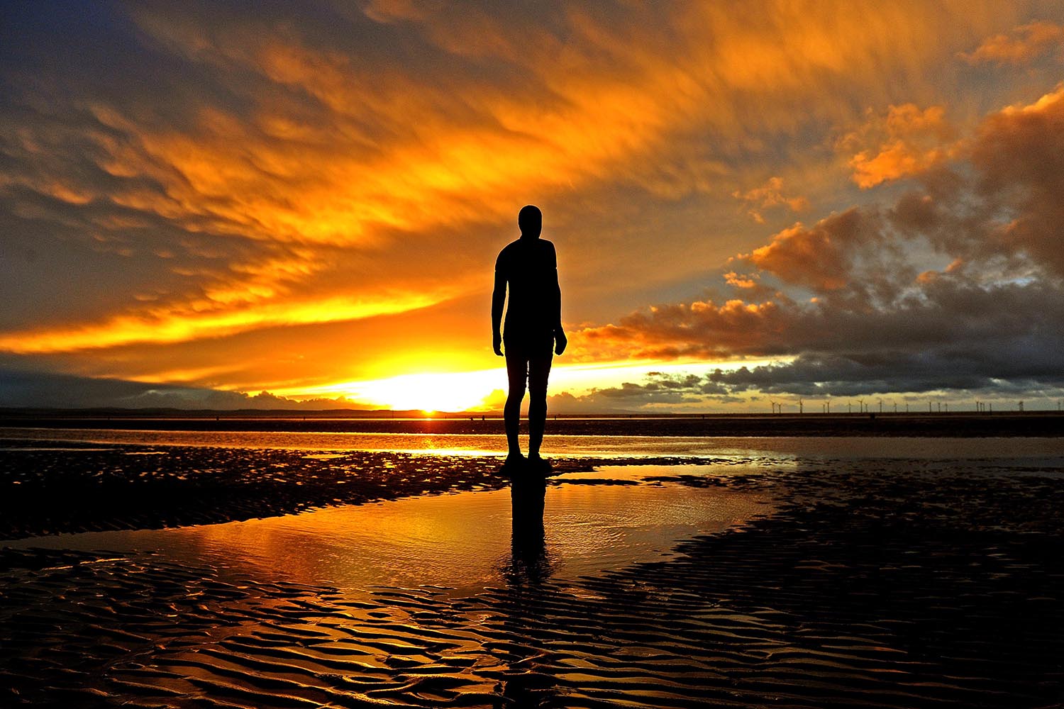 Dramatic shot of one of the 'iron men' in silhouette against the sunset from Antony Gormley's Another Place sculpture installation at Crosby beach in Liverpool. Picture by Gareth Jones.